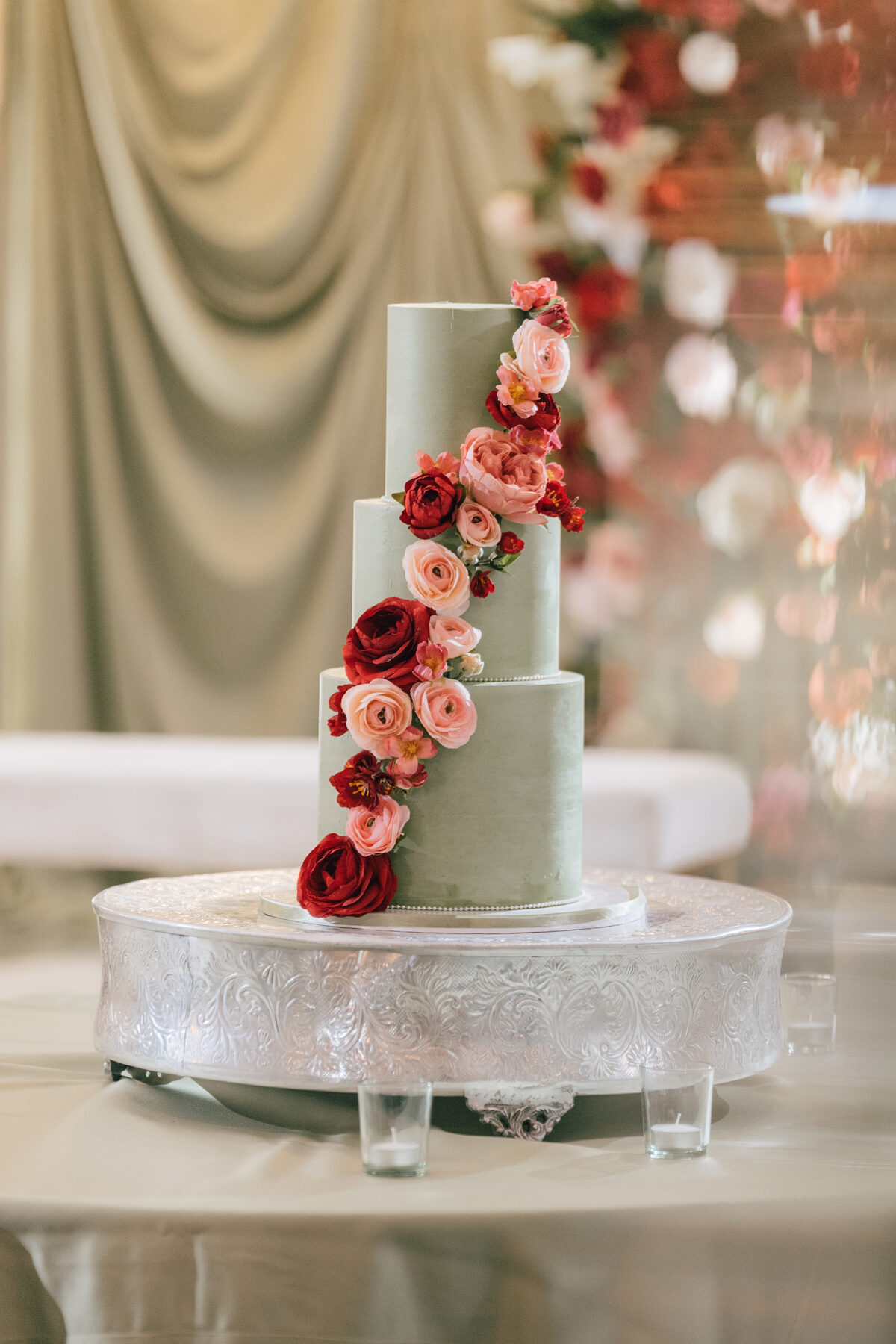 Sage green tiered cake with cascading red and pink roses
